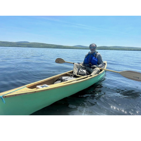 Man in a blue shirt sitting in a green canoe, holding a paddle