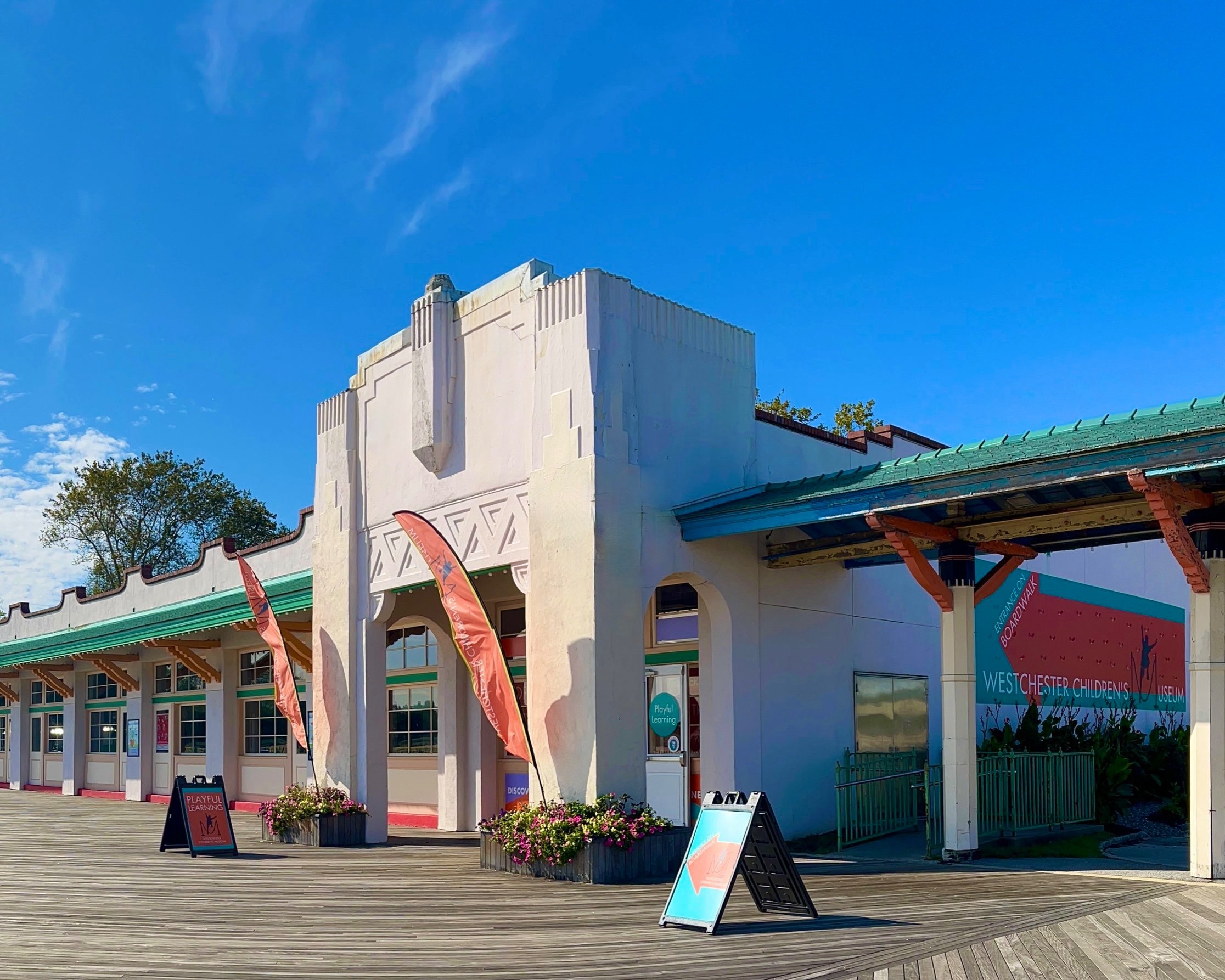 Concrete building with flags and a welcome sign, set against a clear blue sky. 